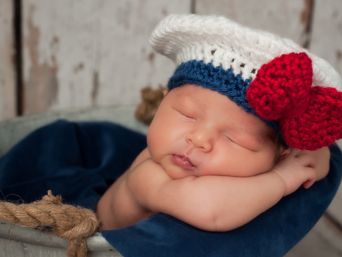 Спящий грудной ребенок в вязаной шапочке с красным бантом