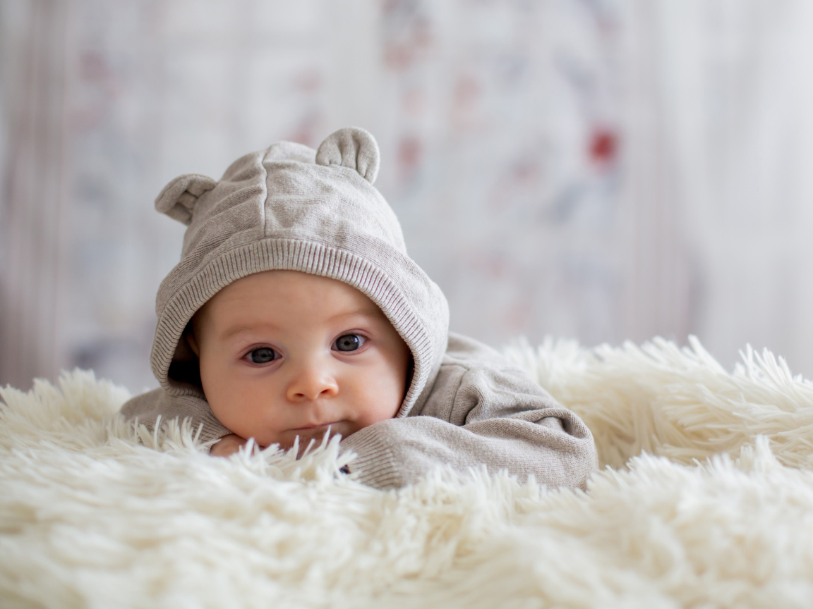 Маленький ребенок лежит на белом меховом покрывале 