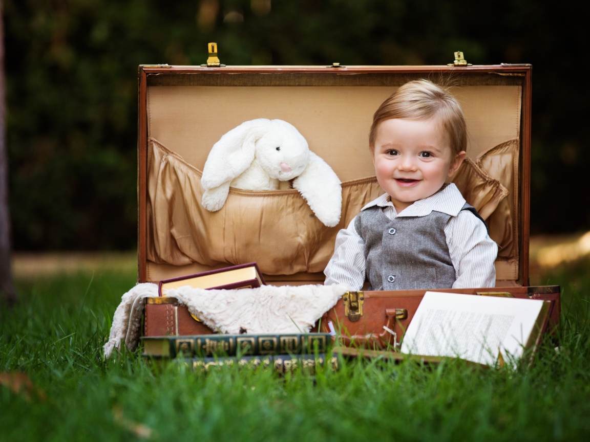 Улыбающийся мальчик сидит в чемодане с книгами