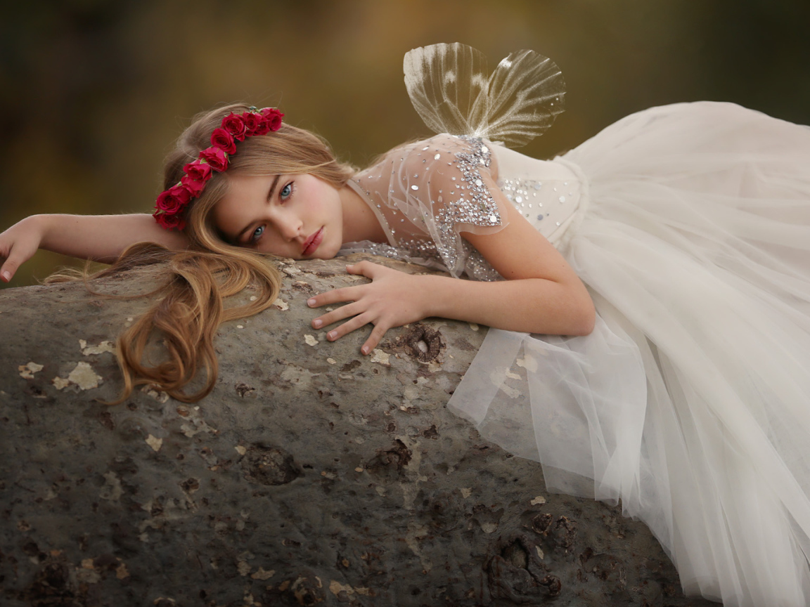 Красивая маленькая девочка в белом платье лежит на камне