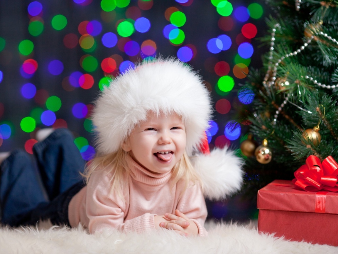 Смешная девочка в новогодней шапке у елки