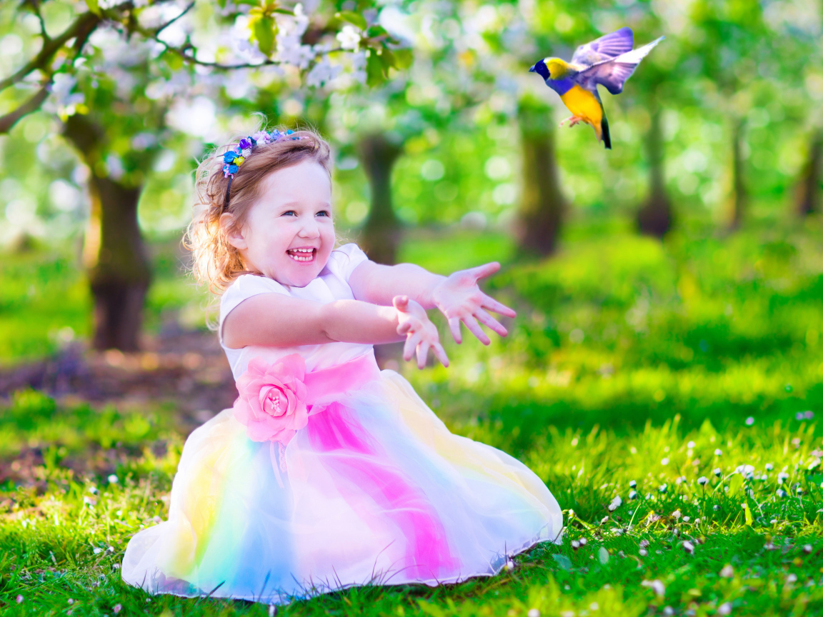 Смеющаяся маленькая девочка в красивом платье на зеленой траве