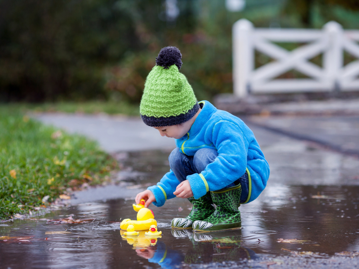 Маленький мальчик с резиновыми уточками в луже осенью