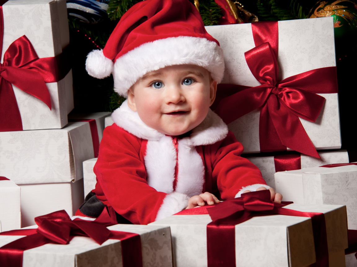Маленький забавный голубоглазый ребенок в костюме Санты сидит на подарках
