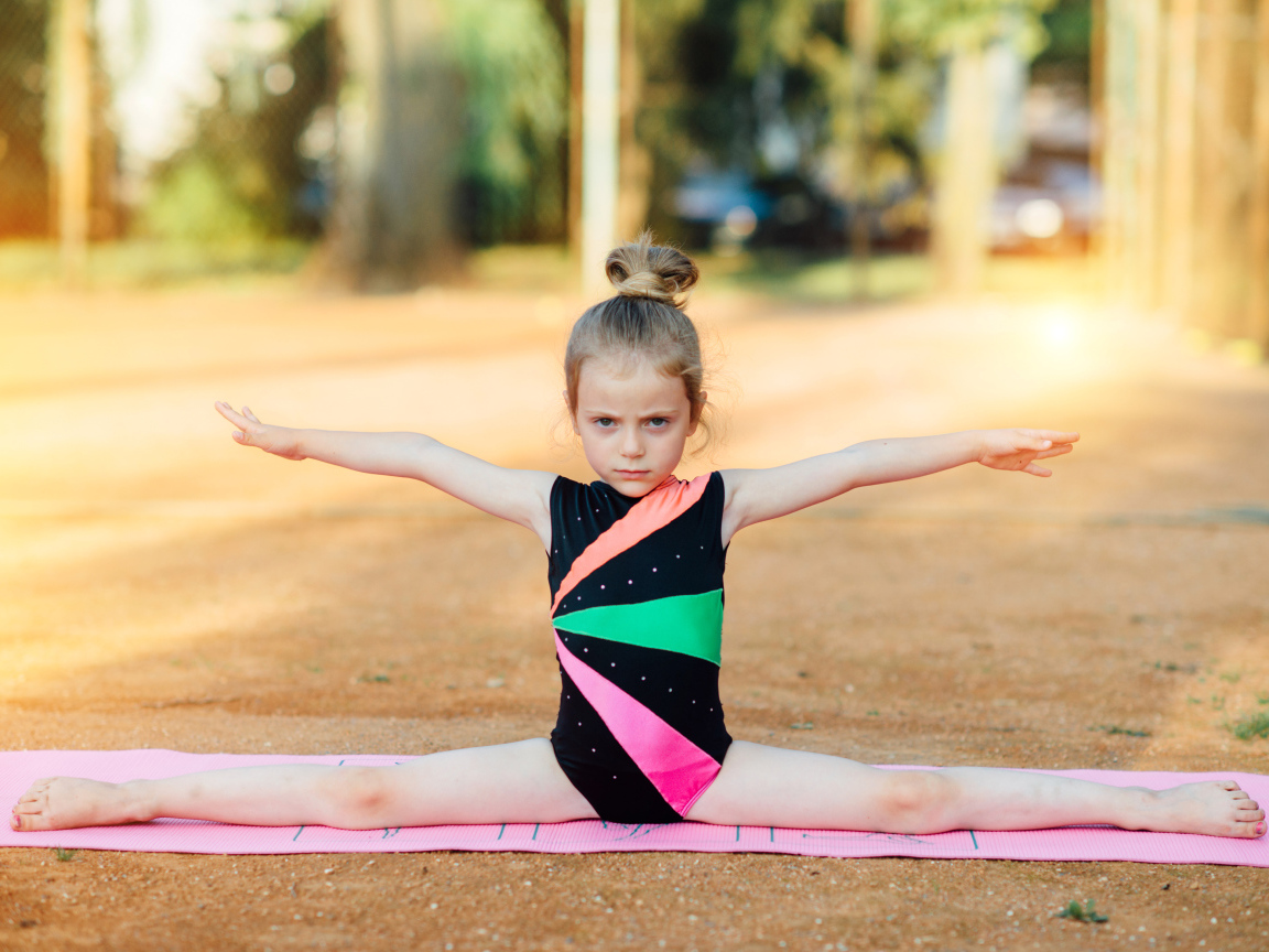 Маленькая девочка гимнастка сидит на шпагате 