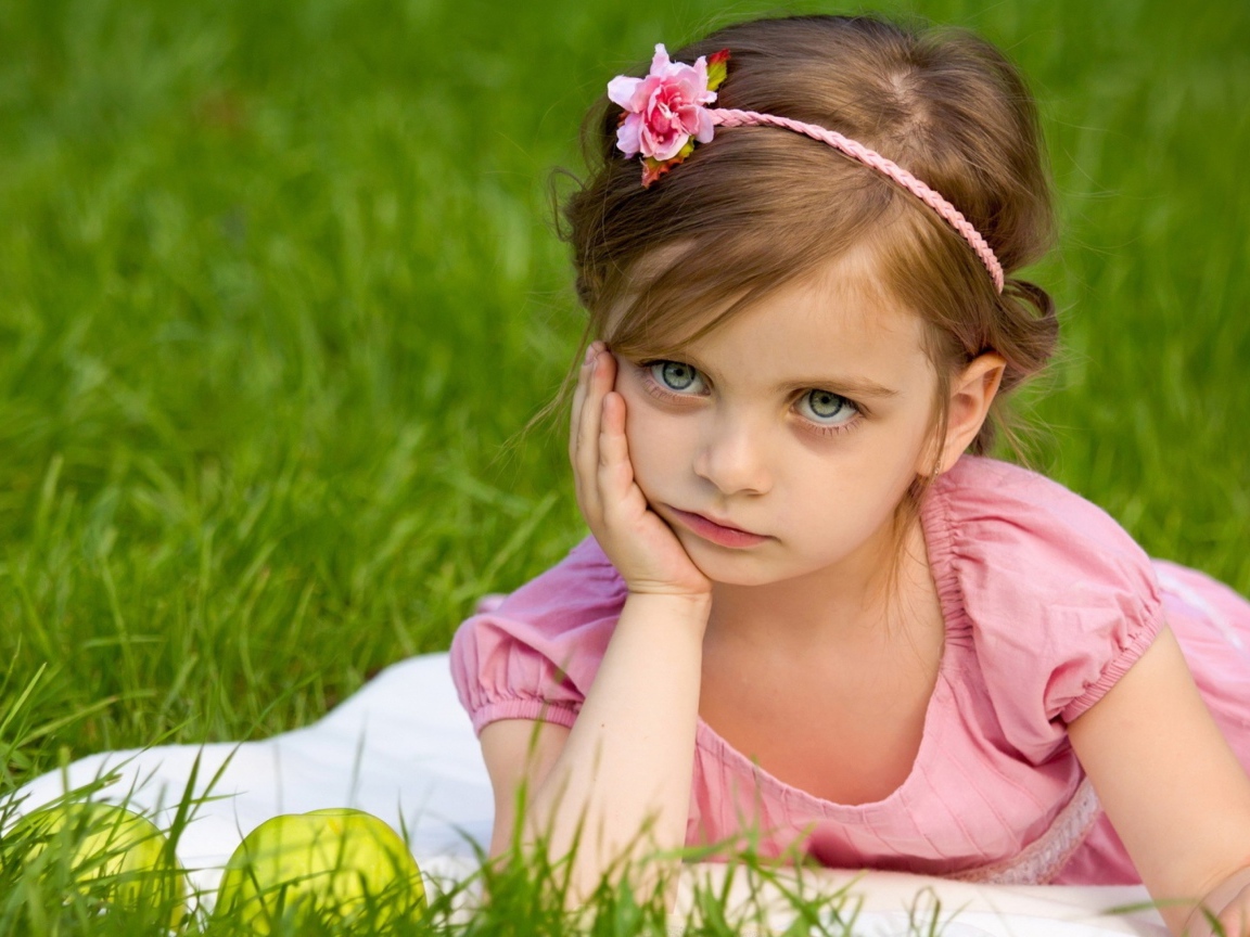 Маленькая девочка в розовом платье лежит на зеленой траве