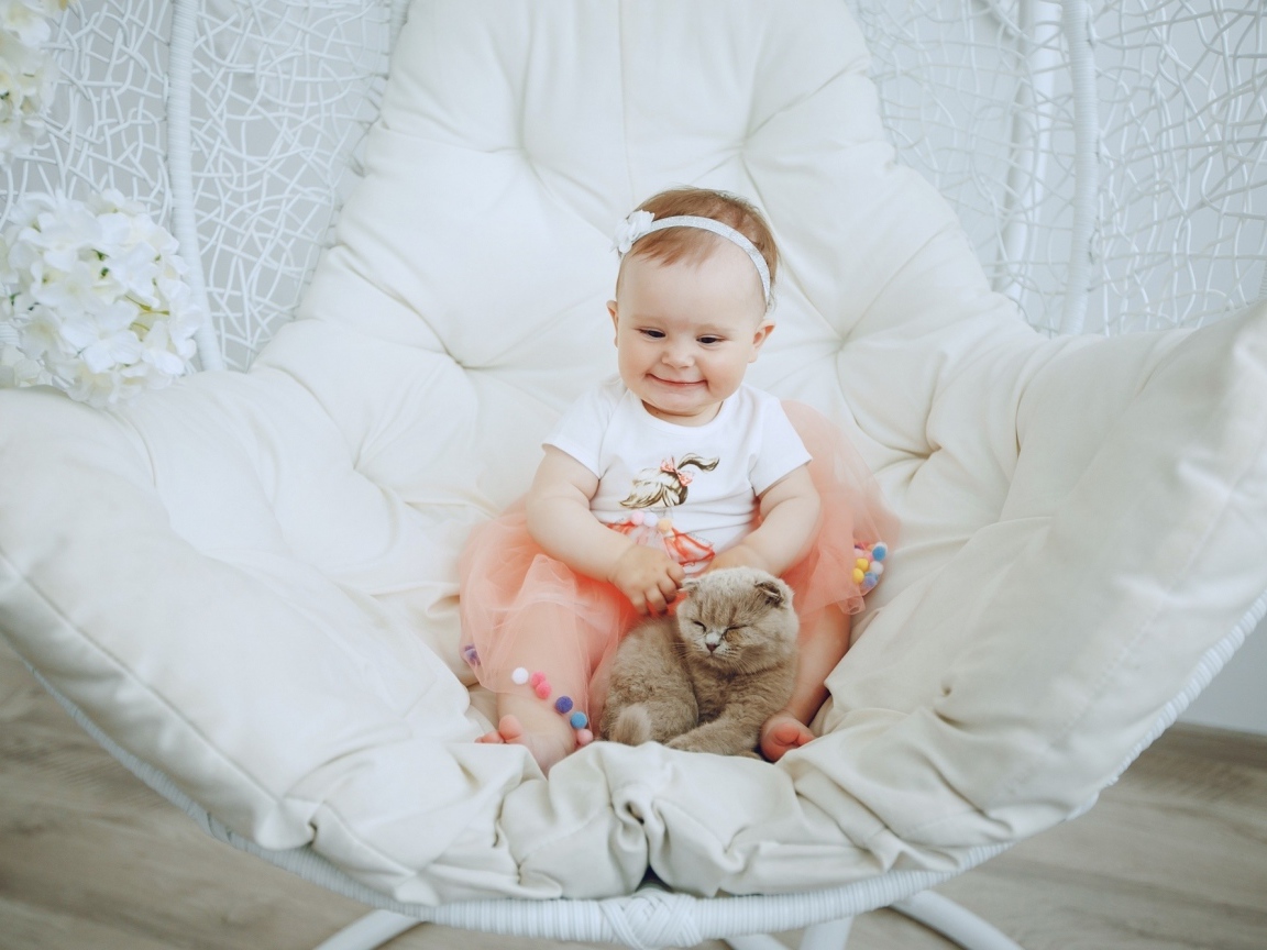 Маленький улыбающийся ребенок с котом сидит в белом кресле