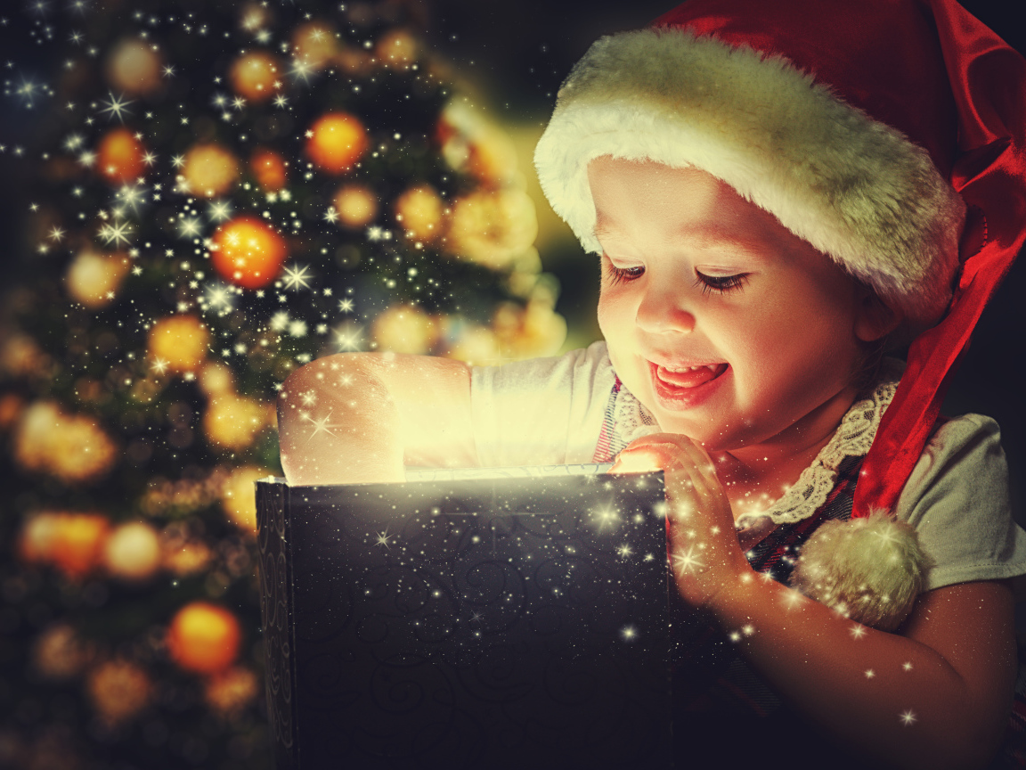 Маленькая улыбающаяся девочка открывает подарок у новогодней елки 