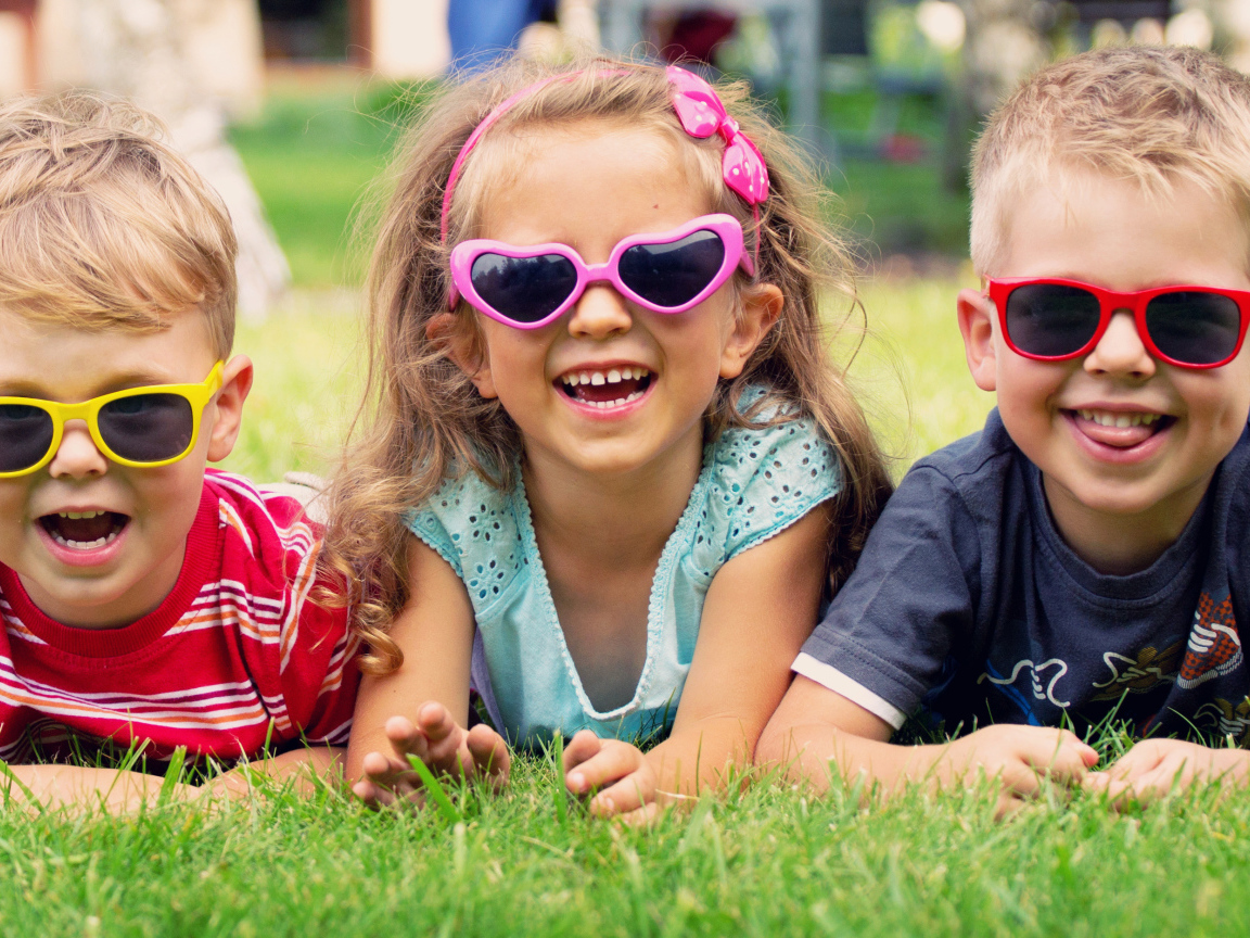 Улыбающиеся мальчики и девочка лежат на зеленой траве