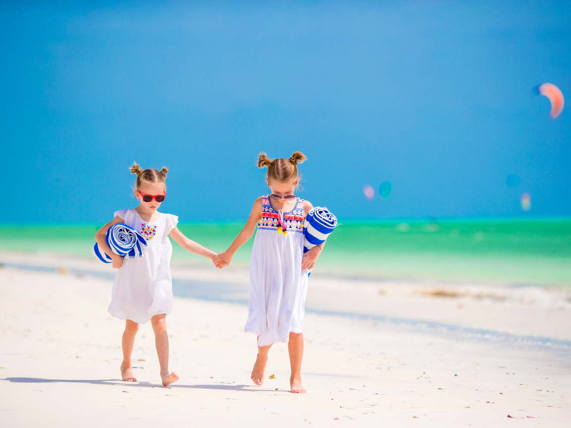Две маленькие девочки идут по песку