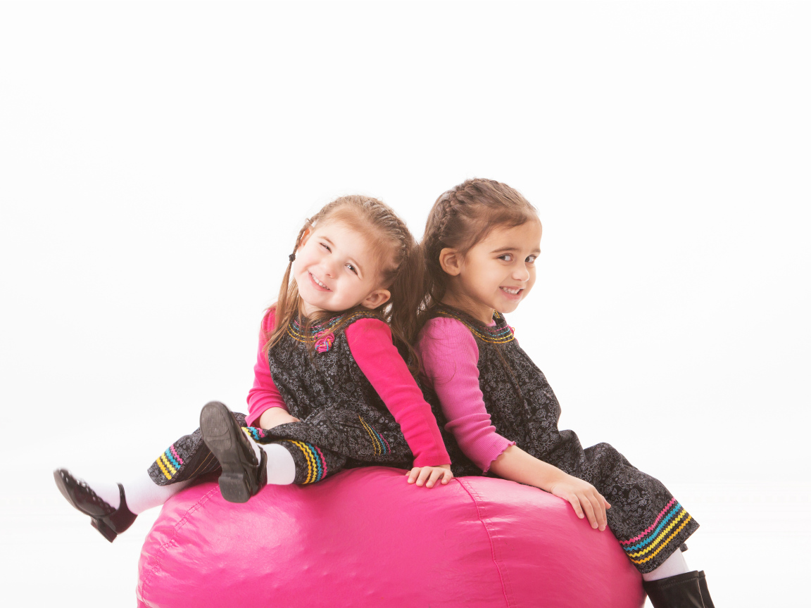 Две маленькие девочки сидят на красном мягком шаре 