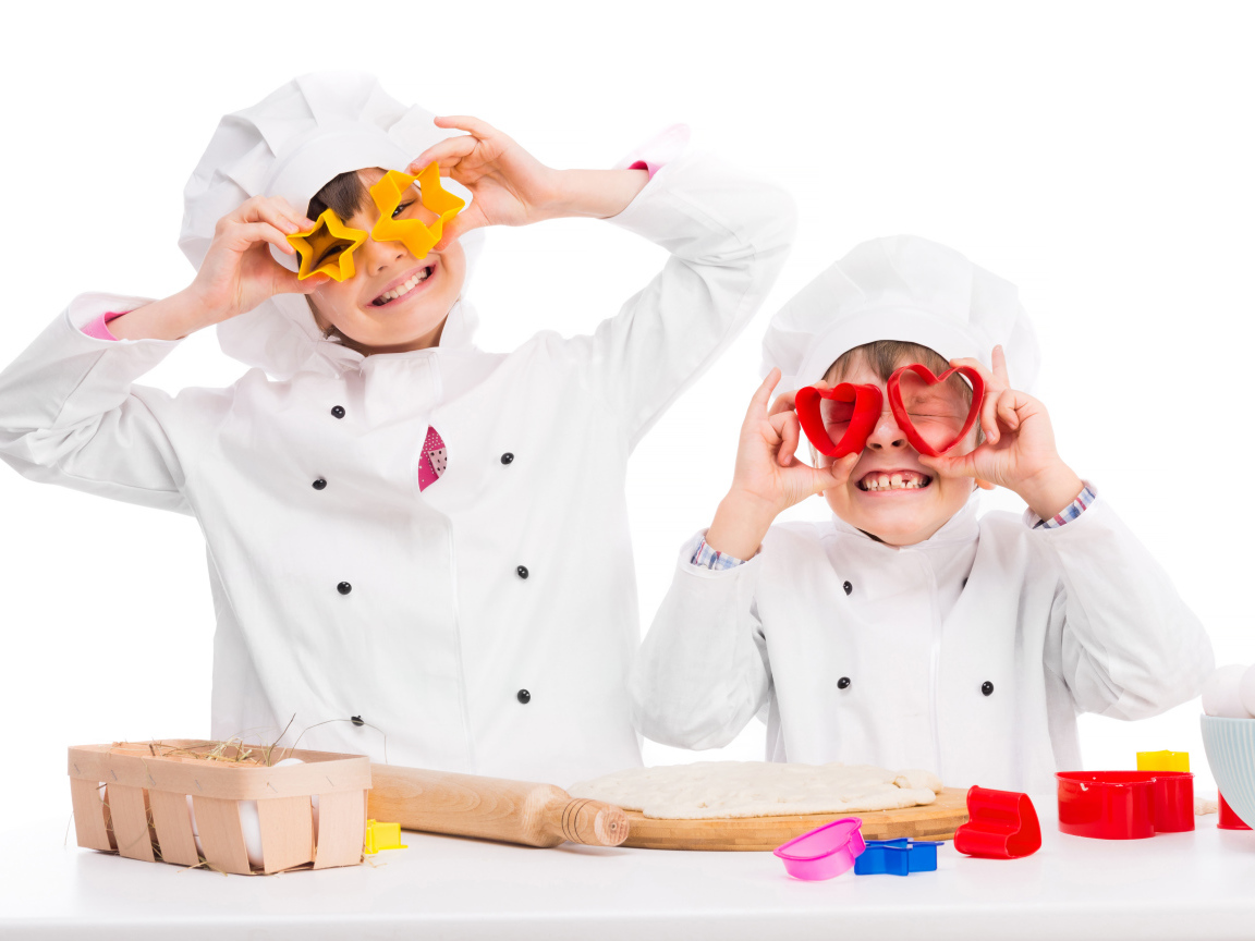 Два маленьких ребенка в костюмах повара готовят на кухне печенье