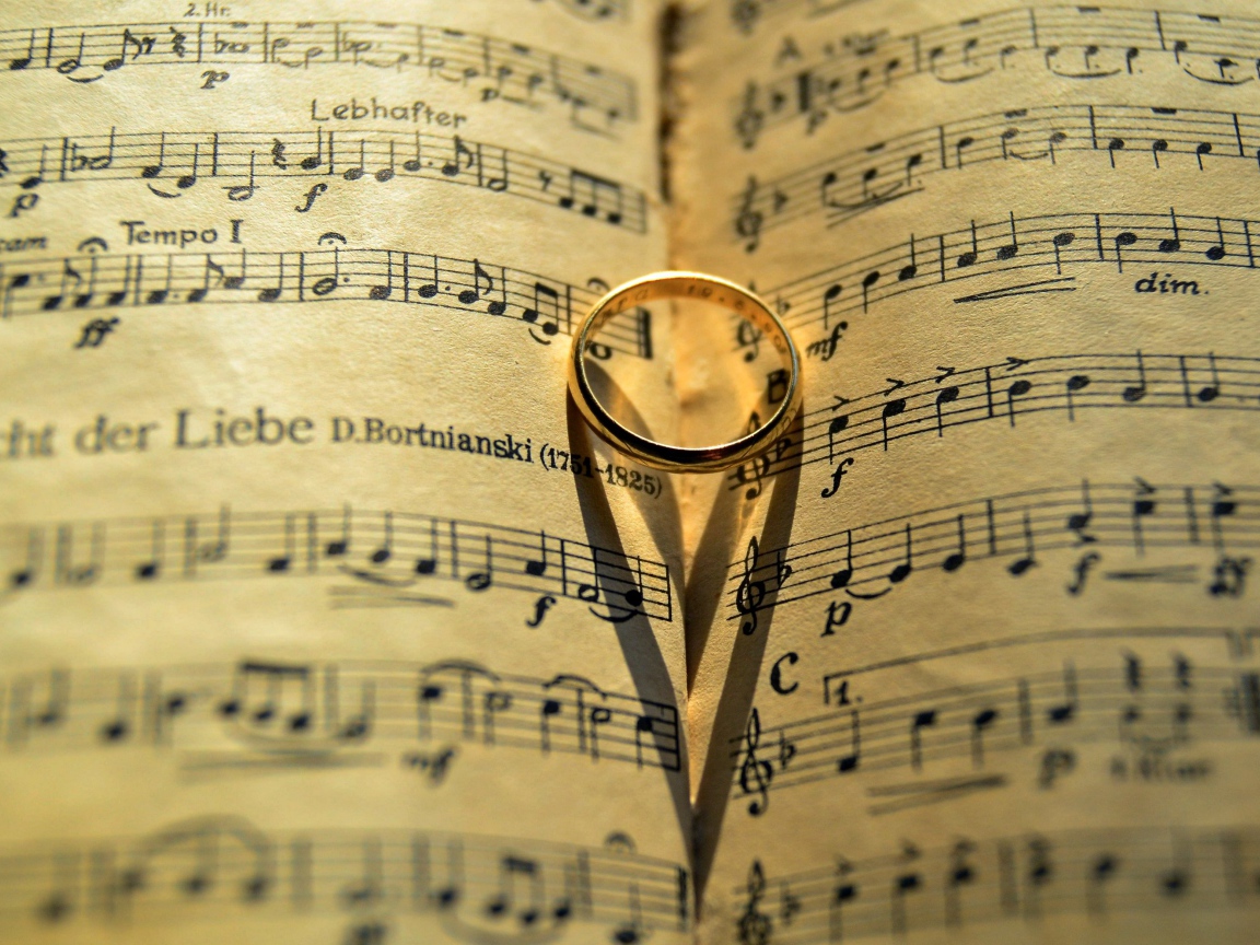 Золотое обручальное кольцо лежит на нотной тетради