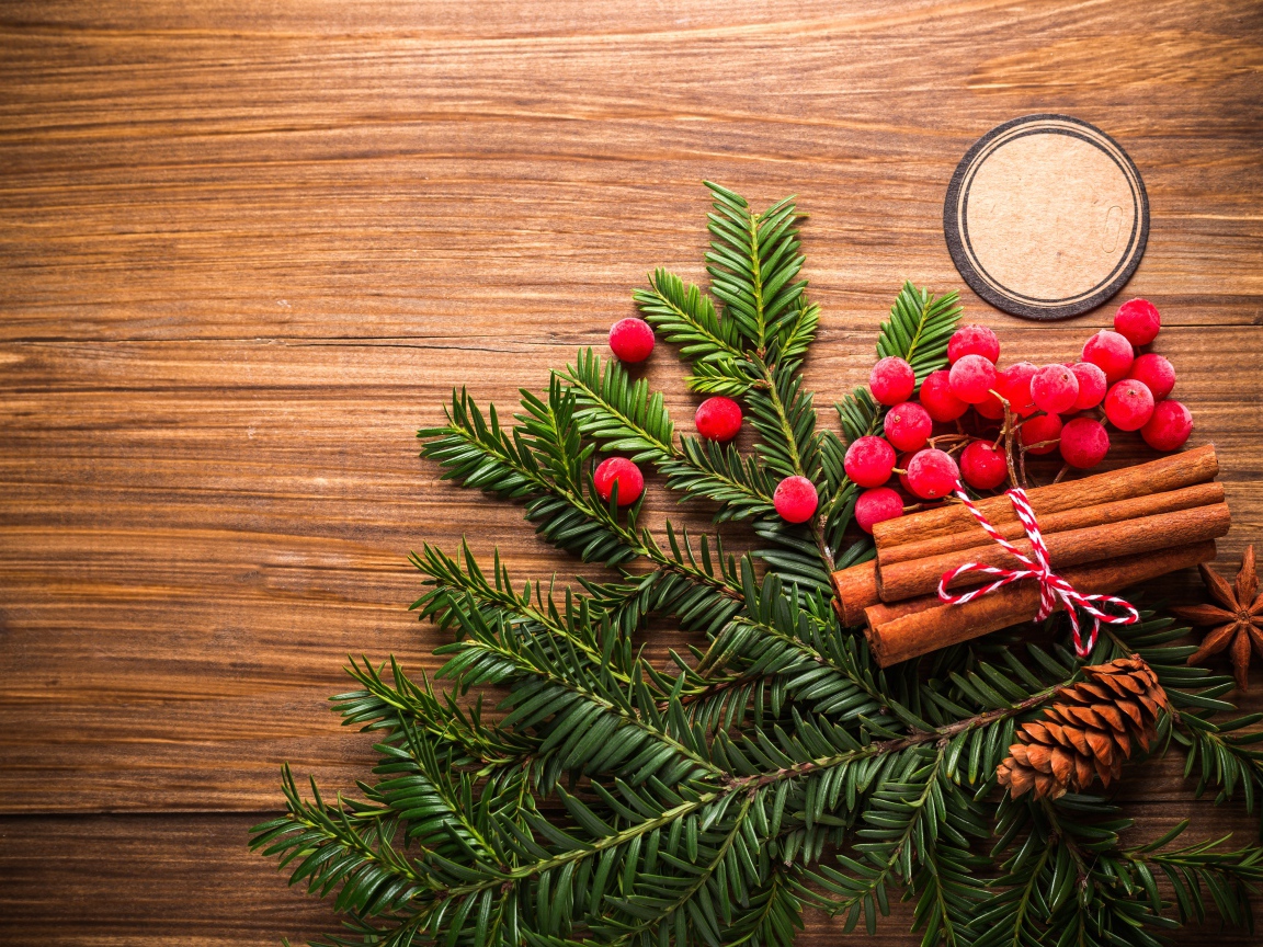 Еловая ветка, корица, ягоды рябины и шишки на деревянном фоне