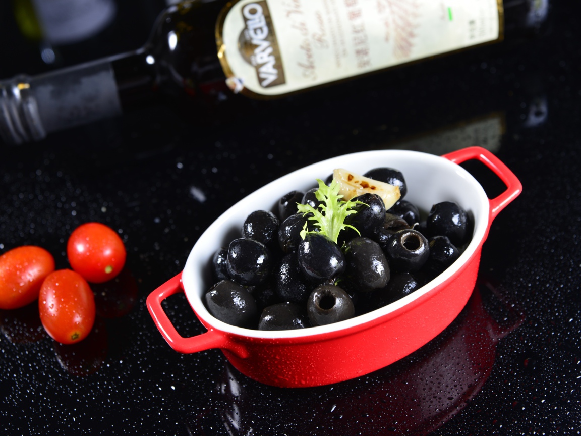 Черные оливки на столе с бутылкой и помидорами