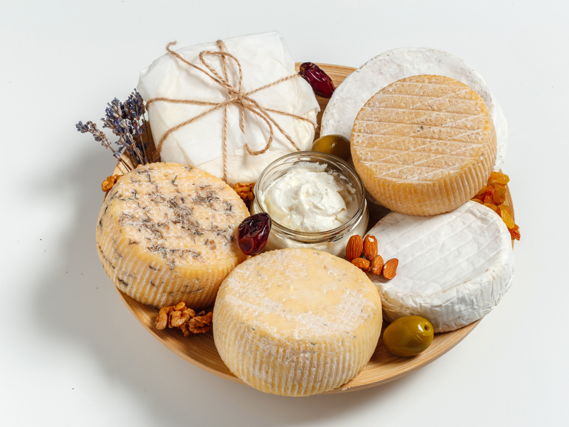 Разные виды сыра на тарелке с орехами на сером фоне