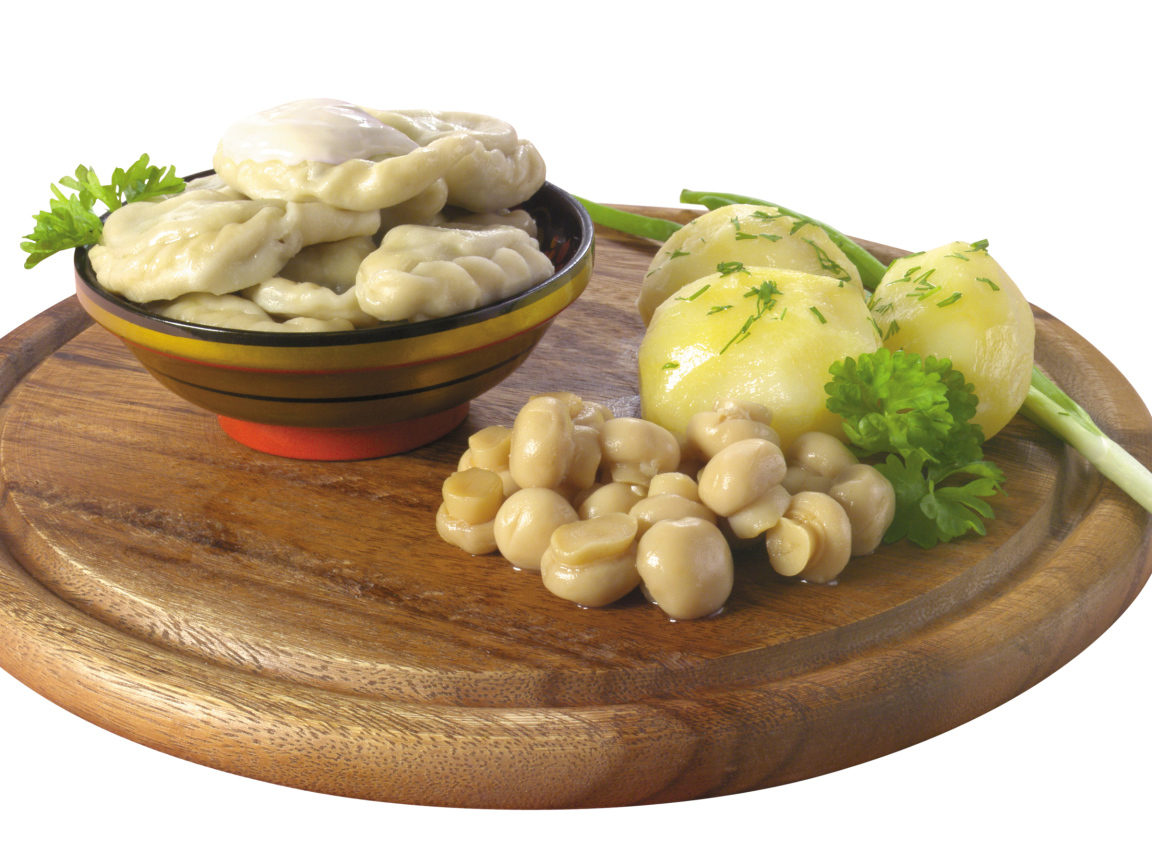 Вареники с грибами и вареной картошкой на деревянной доске на белом фоне
