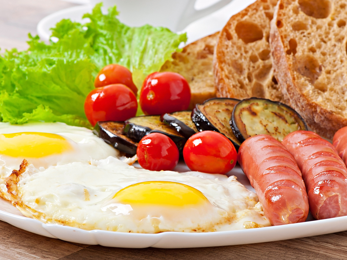 Яичница на тарелке с сосисками, овощами и хлебом