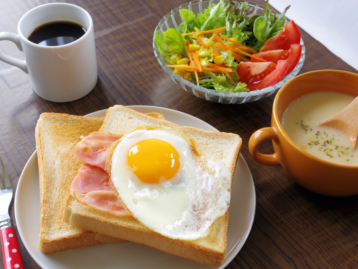 Тосты с яичницей и беконом на столе с салатом, кофе и супом
