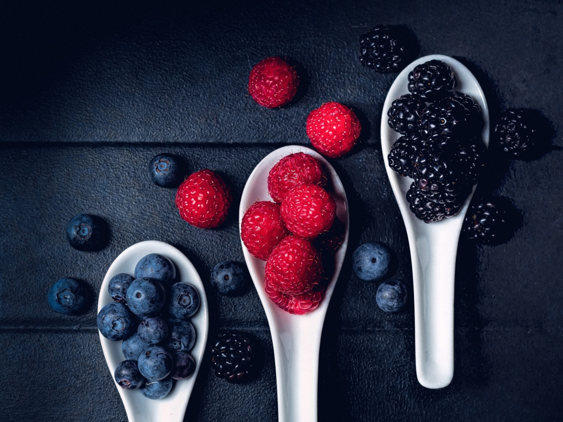 Ягоды черники, малины и ежевики на белых ложках