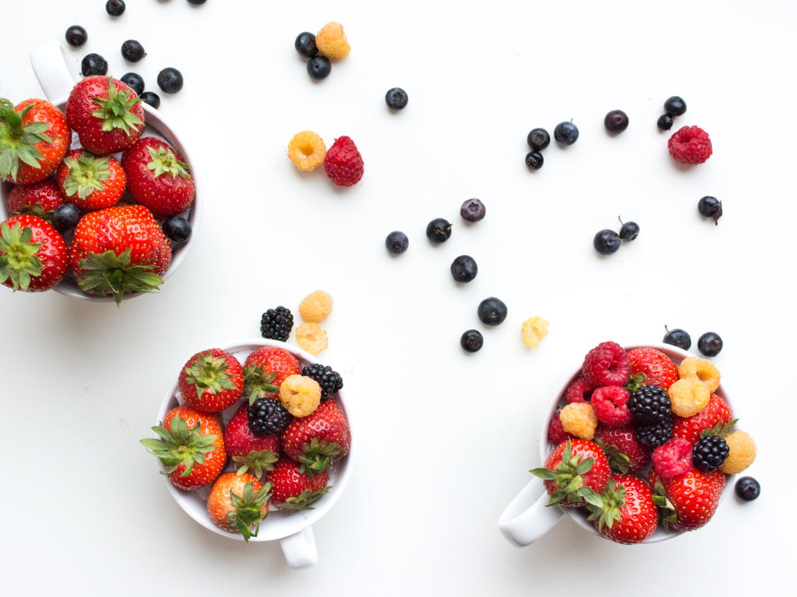 Чашки на столе с ягодами клубники, малины и ежевики 