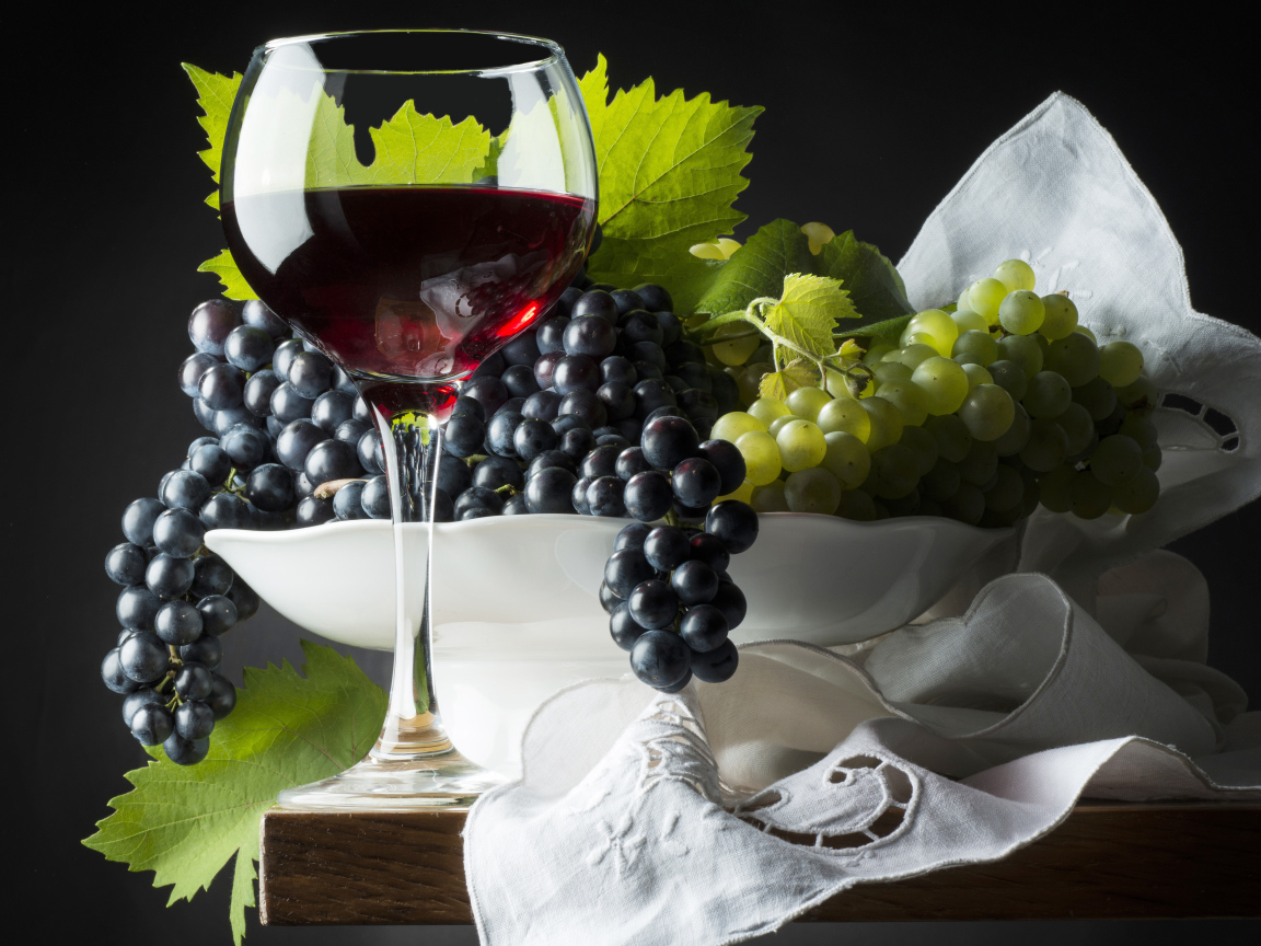Бокал красного вина на столе с белым и синим виноградом