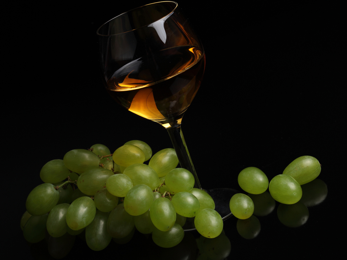 Бокал вина с белым виноградом на черном фоне