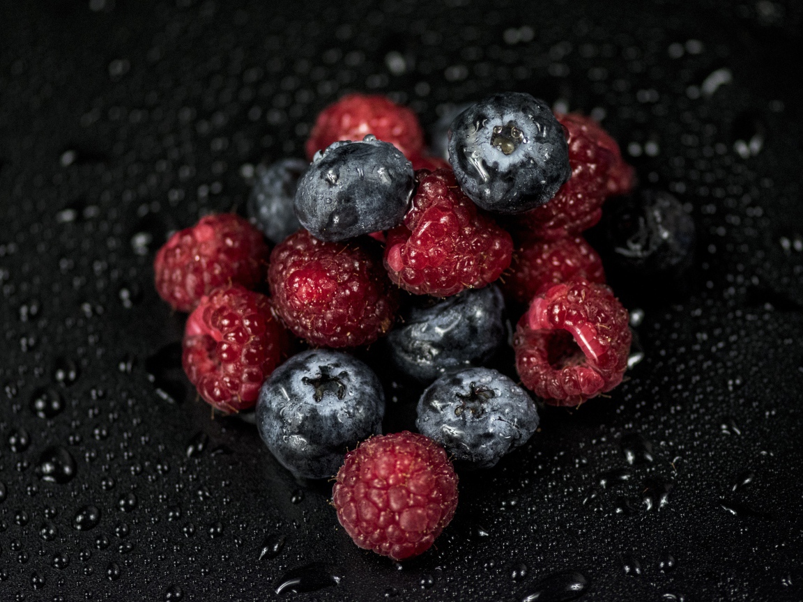 Мокрые ягоды черники и малины на черном фоне
