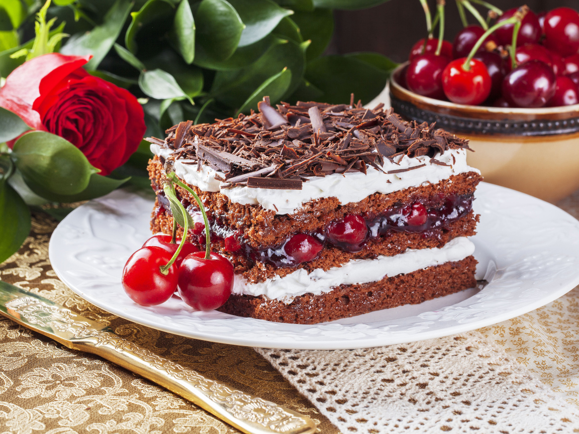 Кусок торта с вишней, шоколадной крошкой на столе с розой