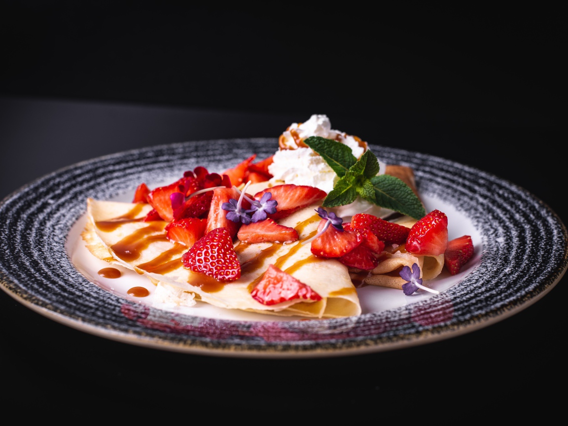 Аппетитные тонкие блинчики с клубникой на черном фоне