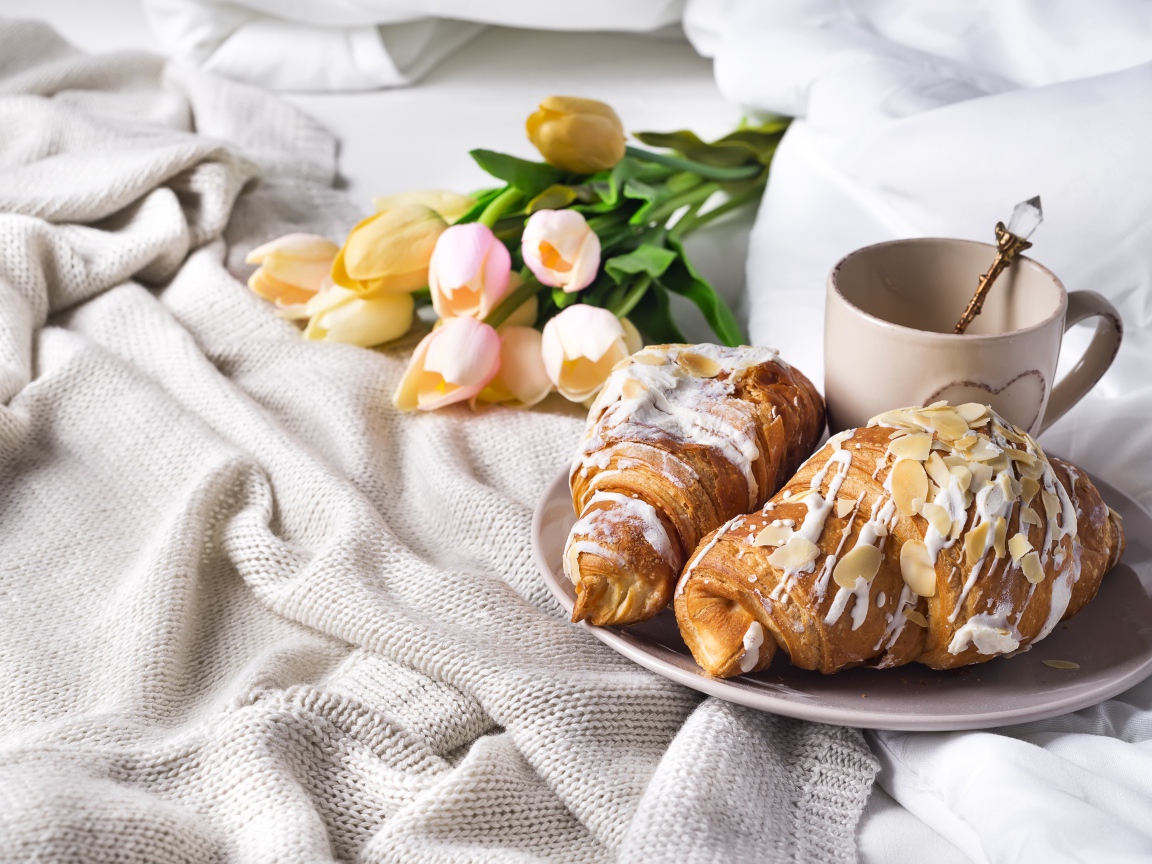 Круассаны на кровати с кофе и букетом тюльпанов