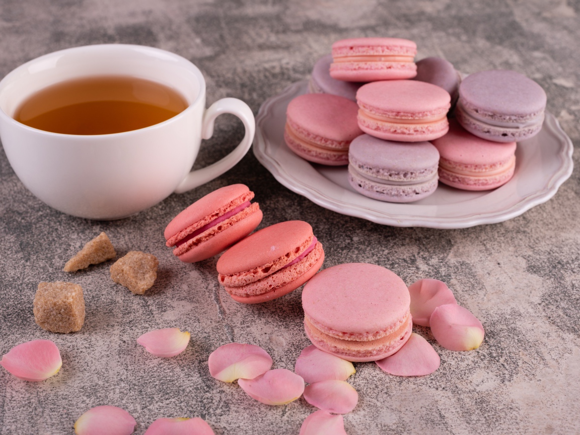 Сладкий десерт макарун на столе с чашкой чая, сахаром и лепестками розы