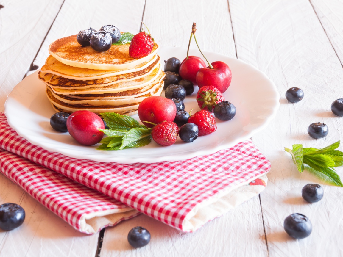 Оладья на белой тарелке с ягодами черники, черешни и клубники