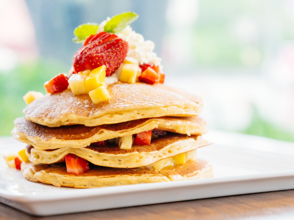 Оладьи с сахарной пудрой, сливками и кусочками клубники и ананаса