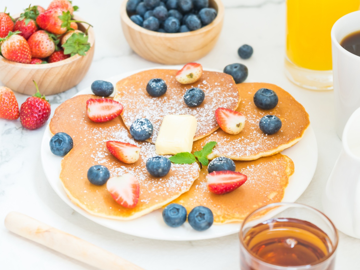 Оладьи с сахарной пудрой, клубникой и черникой на столе
