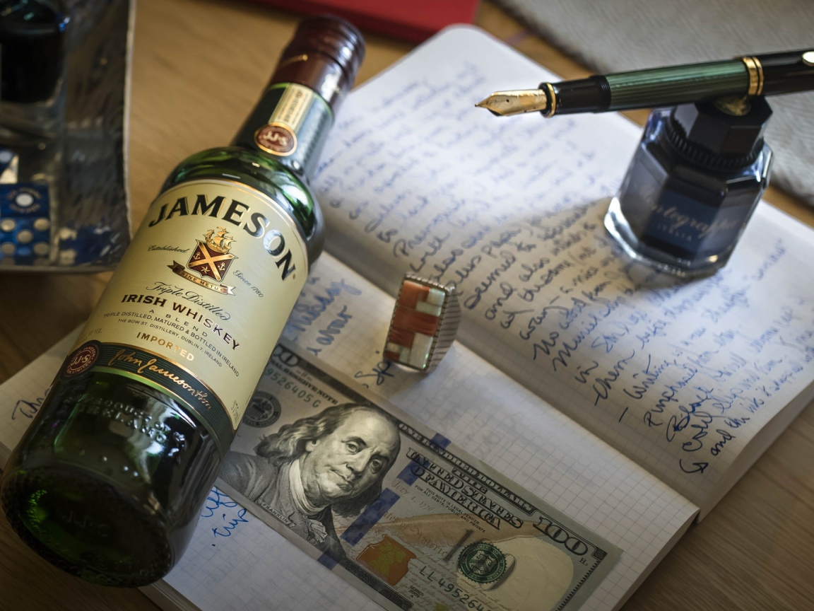 Бутылка виски лежит на тетради с чернильницей и купюрой