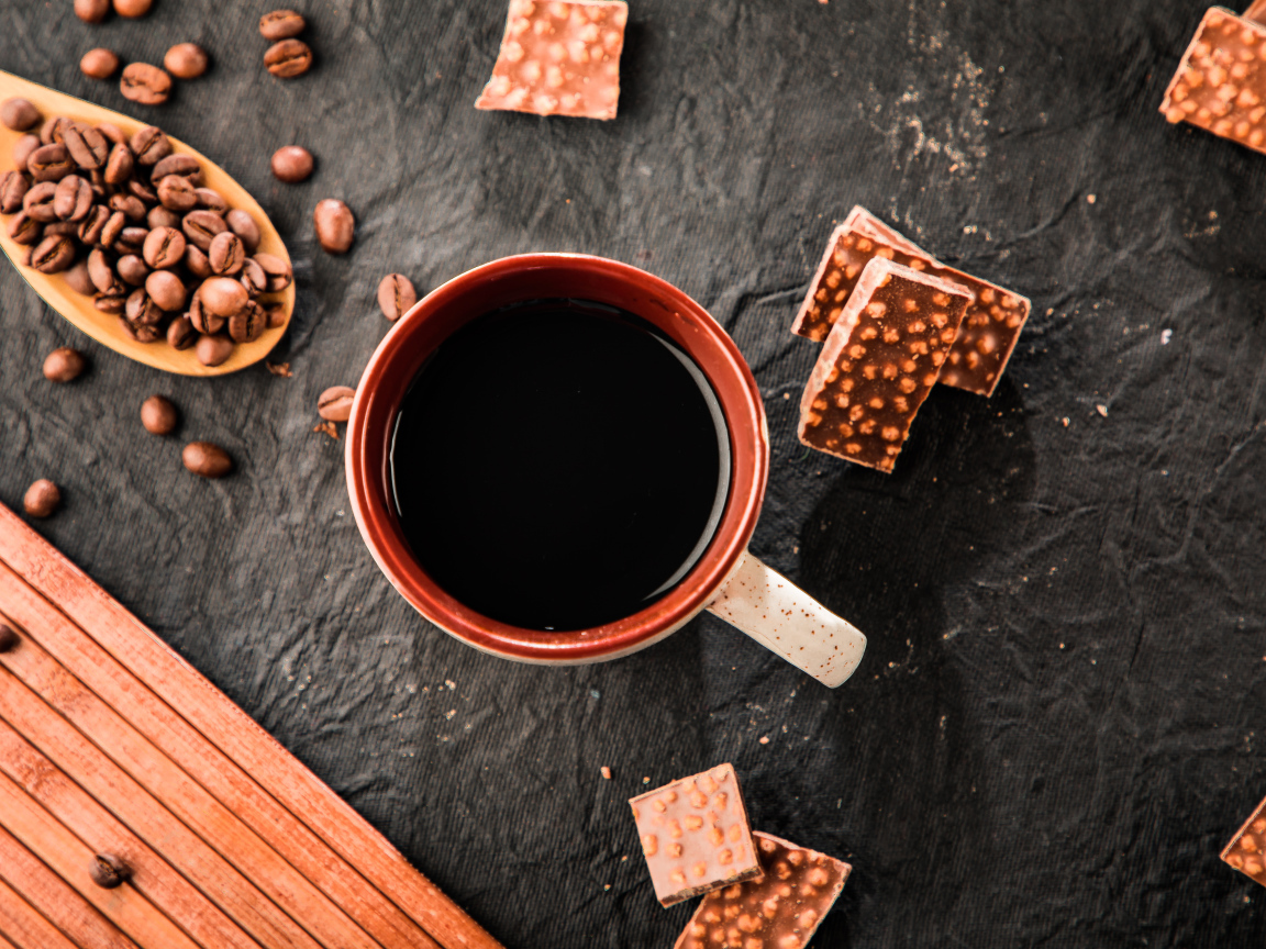 Чашка кофе на столе с кусочками шоколада и кофейными зернами