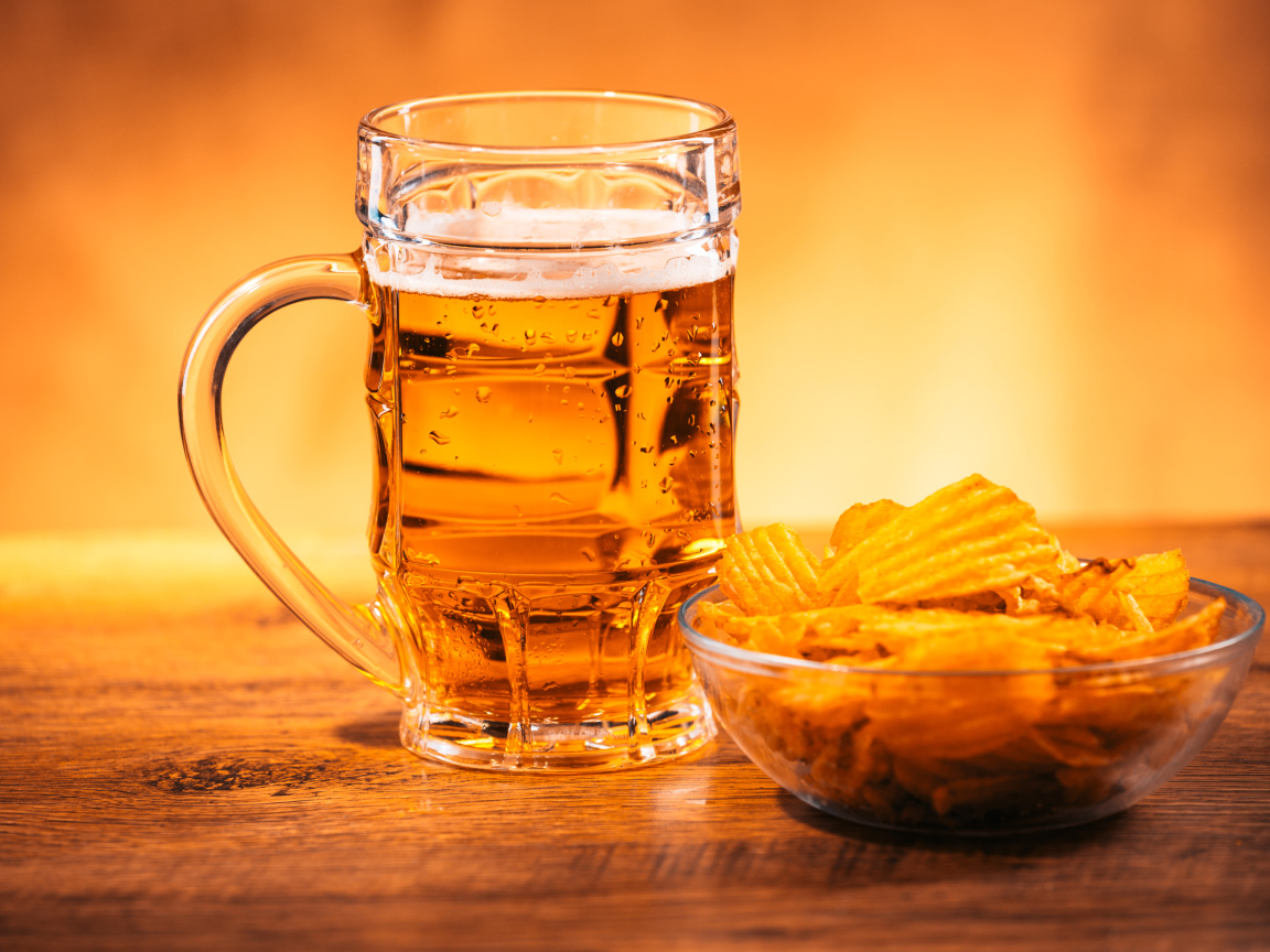 Бокал пива с тарелкой чипсов на столе 