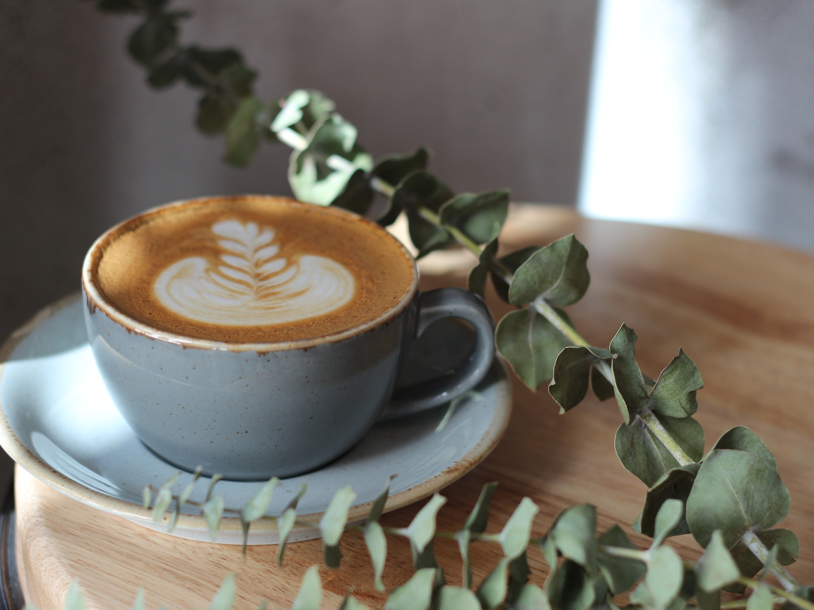 Большая чашка кофе с рисунком на пене на столе с веткой