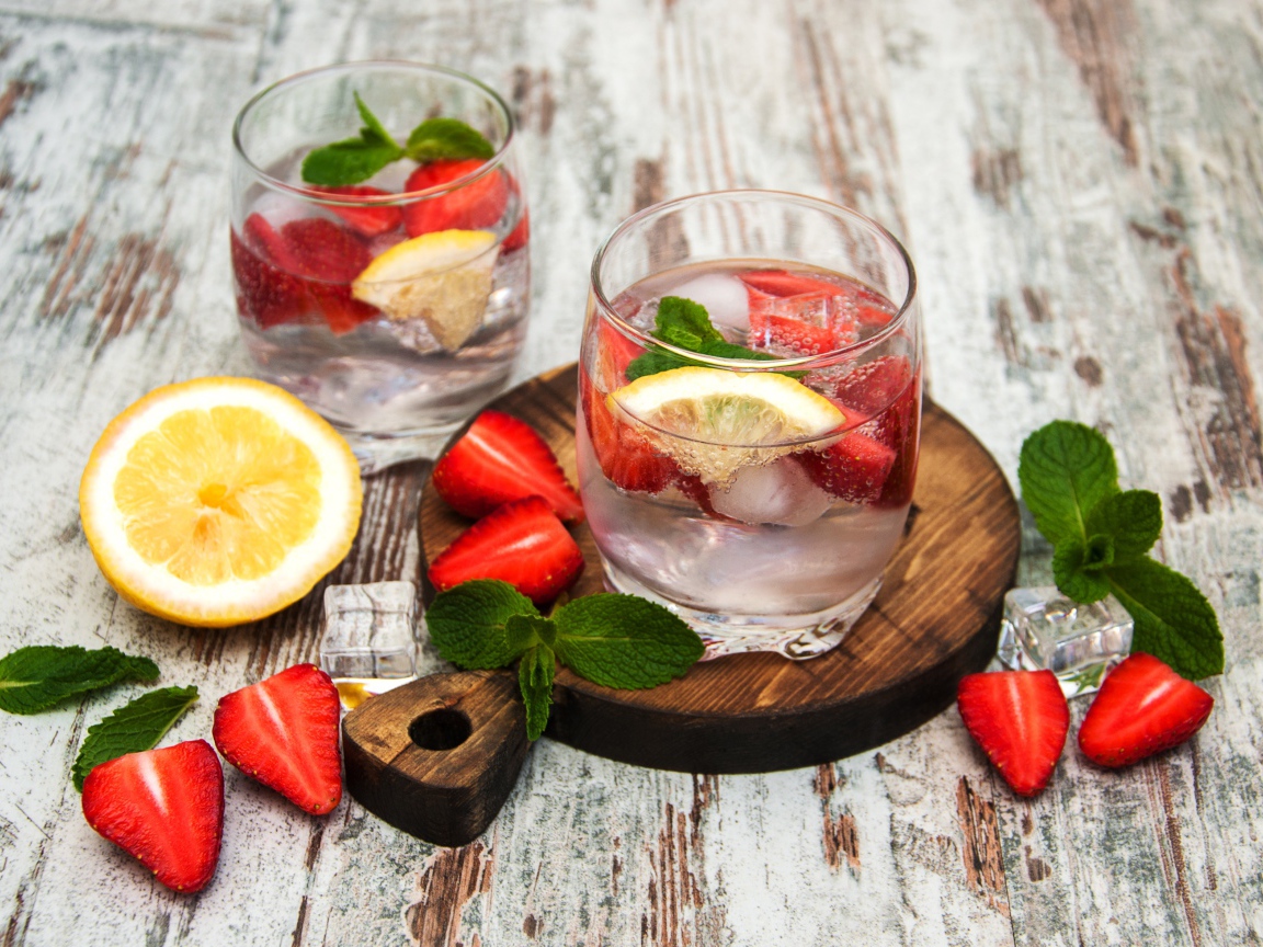 Холодный мохито на столе с ягодами клубники, лимоном и мятой