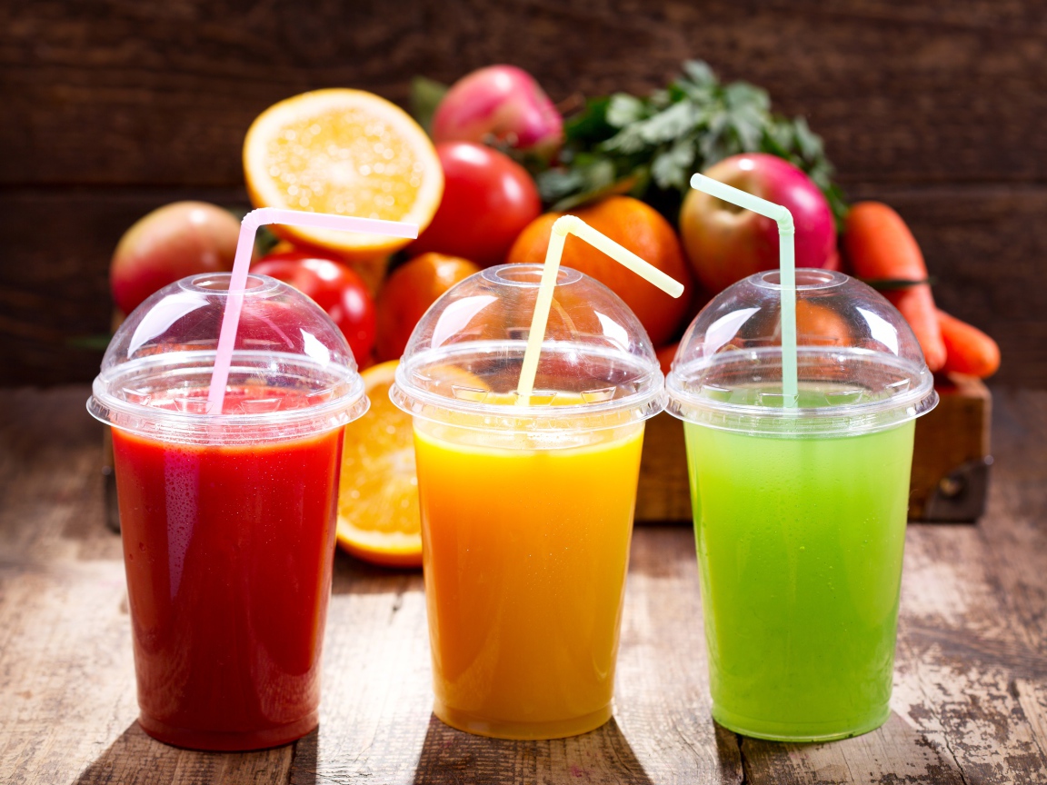 Свежие соки в стаканах с трубочками на столе