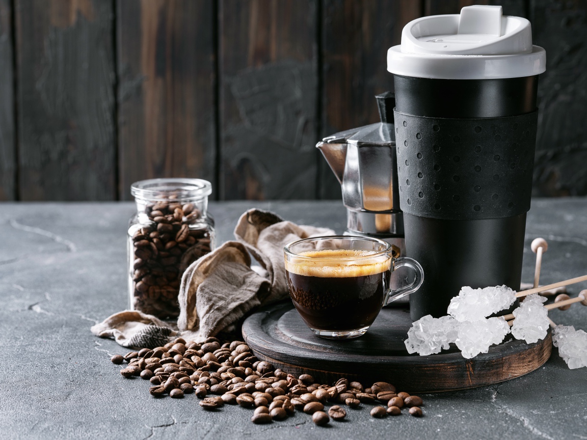 Стеклянная чашка кофе на столе с термосом и зернами