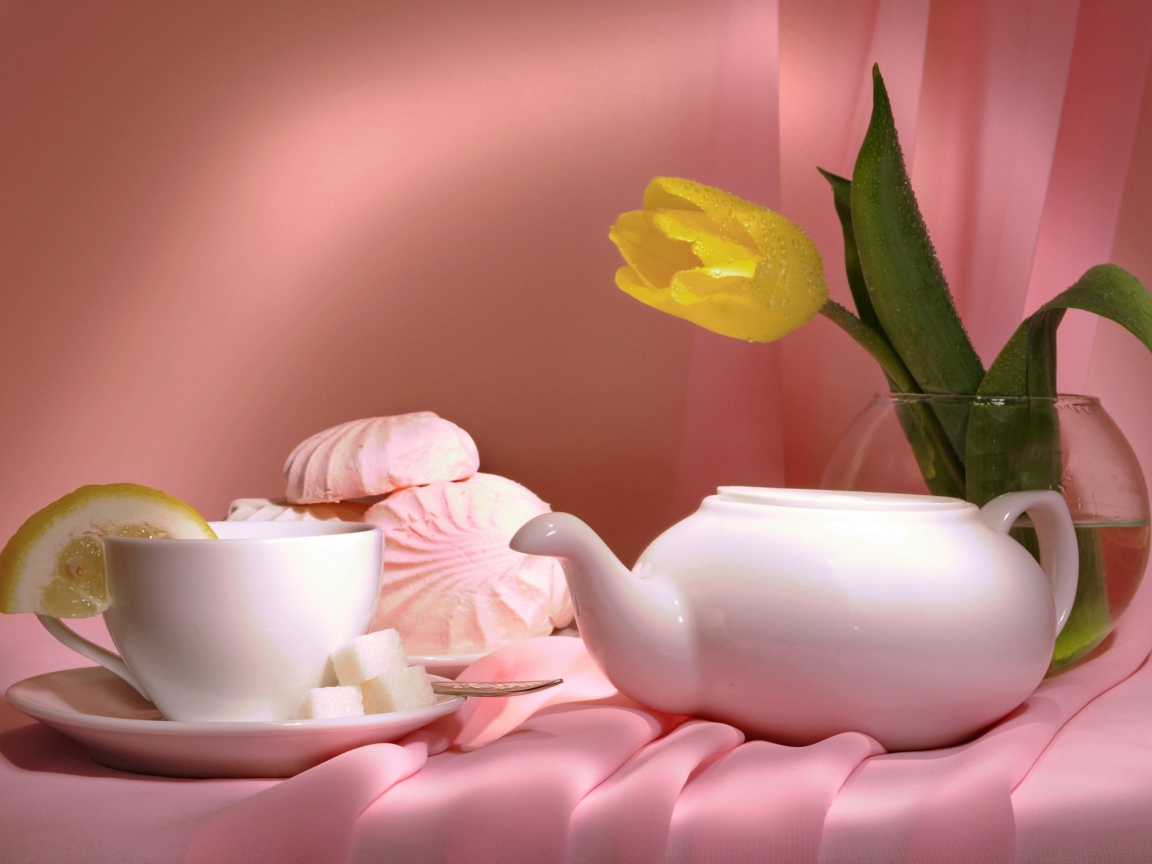 Чайник на столе с чашкой, зефиром и желтым тюльпаном