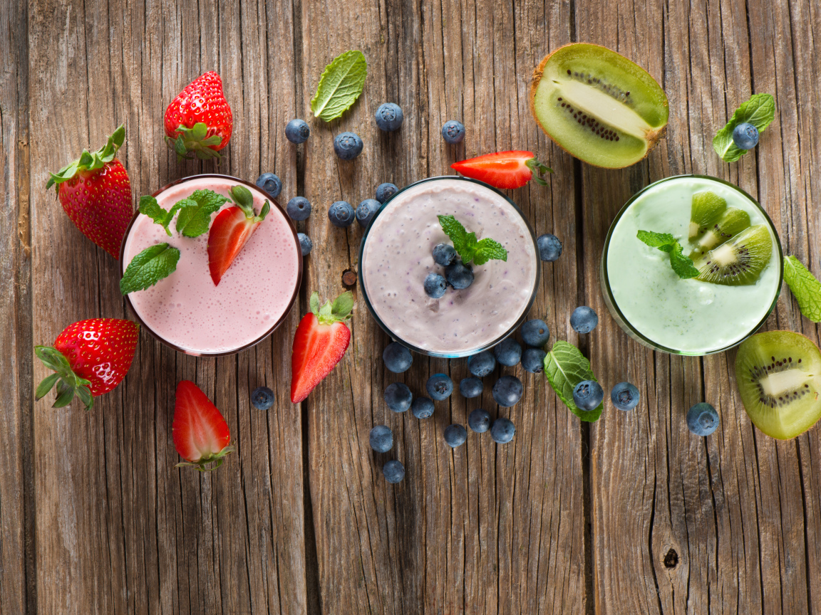 Стаканы со смузи на столе с киви, ягодами клубники и черники