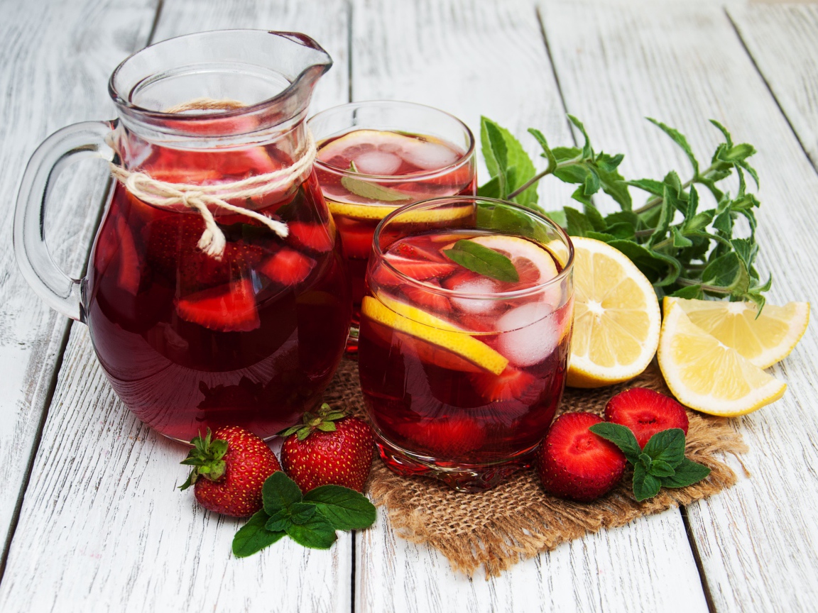 Два стакана мохито на столе с графином, лимоном, клубникой и мятой