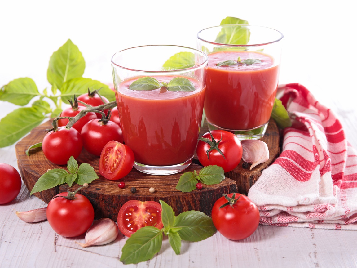 Два стакана томатного сока на столе с помидорами и зеленью 