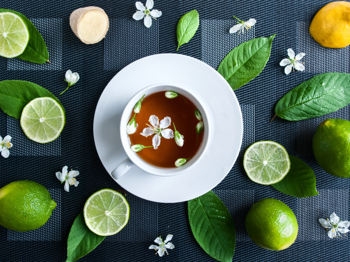 Белая чашка с чаем на столе с лаймом и зелеными листьями 