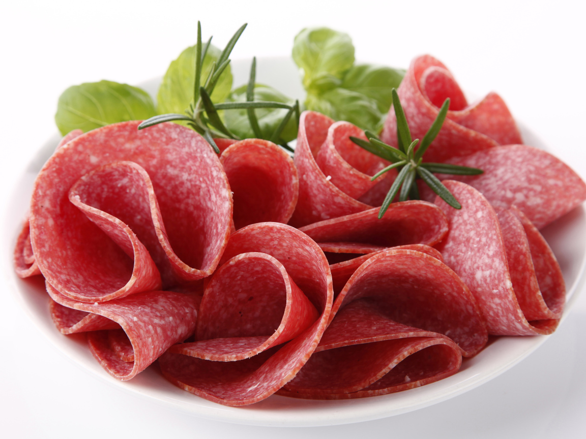 Тонкие кусочки колбасы на тарелке с зеленью 