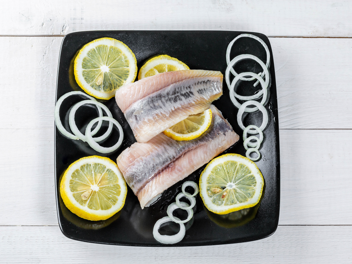 Филе сельди на черной тарелке с луком и лимоном