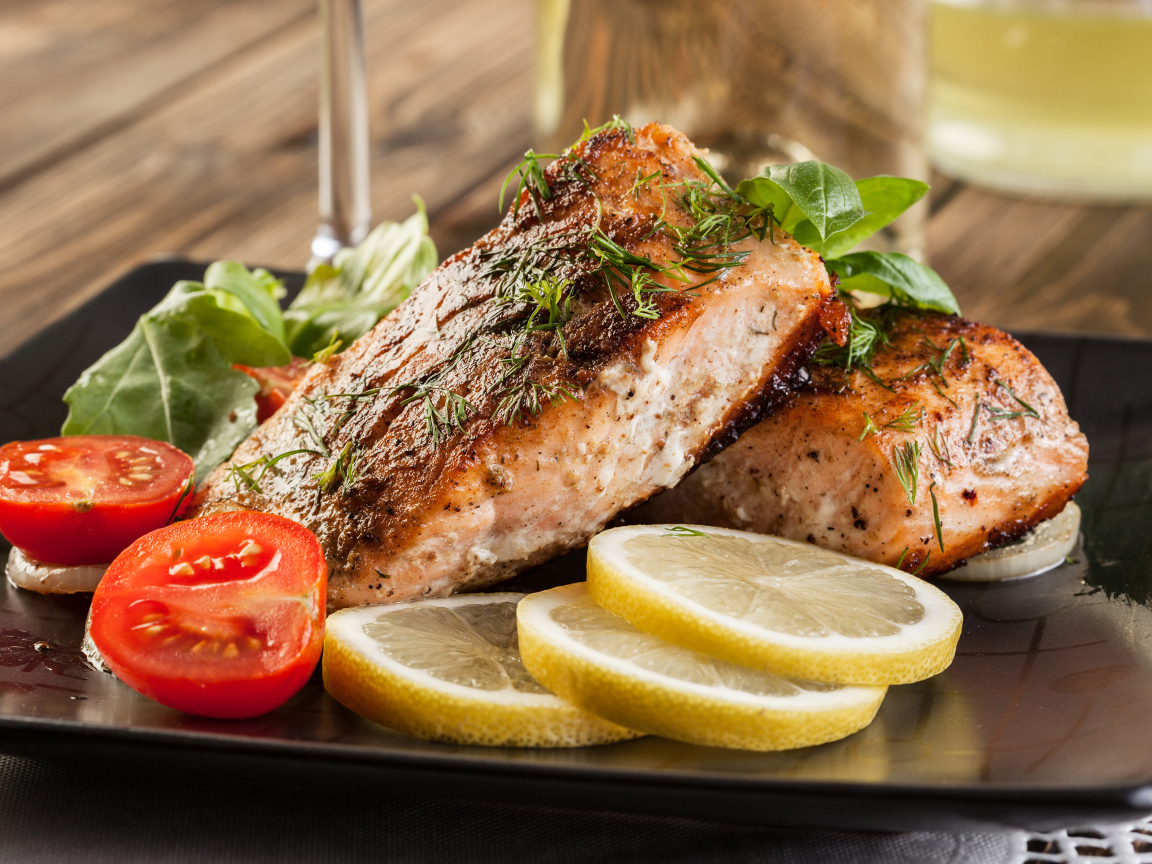 Куски запеченной рыбы на тарелке с помидорами и лимоном